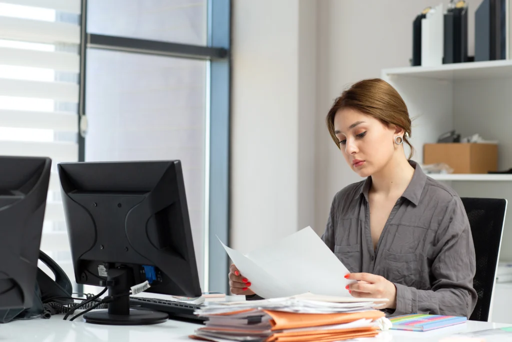 A woman sits at a desk in an office, reviewing documents for an SEO audit service Delhi.